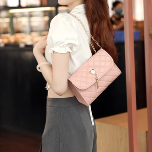 Pink quilted crossbody bag with golden chain strap and a cat head pearl tassel charm