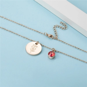 Rose gold necklace with carnation flower pendant and red birthstone on light blue background