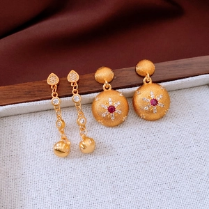 Detail of 24k gold-plated round earrings with red gemstone and textured sunburst design