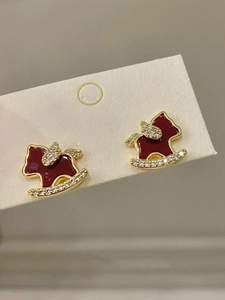Macro view of gold-plated rocking horse earrings with red enamel and white zircon details