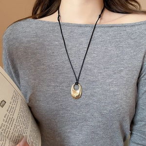 Pendentif ovale doré minimaliste sur cordon noir porté avec un haut en maille