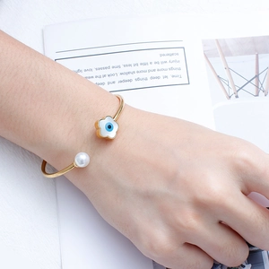 Detail of gold open cuff bracelet featuring pearl and blue evil eye flower charm