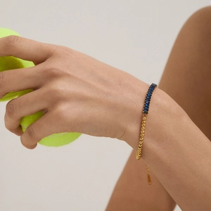 Detail of gold beaded bracelet with blue rectangular gemstone on model wrist