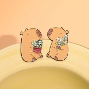 Set of two cartoon capybara enamel pins holding plants and flowers on orange background