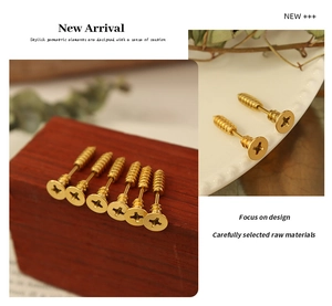 Macro shot of gold-plated screw earrings displayed on red wood and ceramic tray