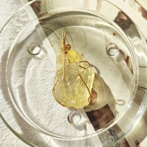 Macro view of natural yellow crystal pendant wrapped in golden wire on linen fabric