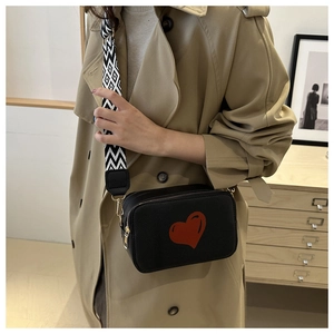 Detail of black crossbody bag with red heart pattern and geometric patterned wide strap