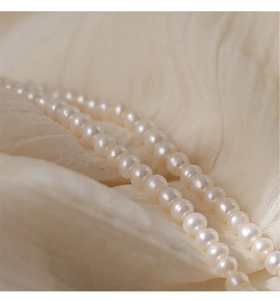 Detail shot of natural white pearl necklace with gold beads on elegant silk fabric