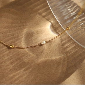 Detailed view of 18K gold plated chain with white pearl and beads on sand background