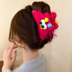 Plush monster hair claw clip with colorful pom-poms and eyes worn on a woman's hair