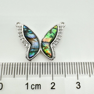 Détail macro d'un pendentif papillon avec nacre d'abalone et cristaux près d'une règle