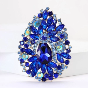 Macro detail of gold-tone brooch featuring a pear-cut blue crystal and rhinestone accents