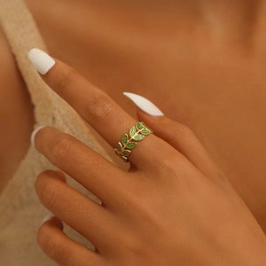 Detail of adjustable gold-plated titanium ring with green enamel leaf pattern on finger