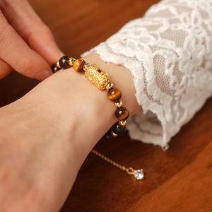Detailed close-up of tiger eye stone bracelet with golden cylinder charms and crystals