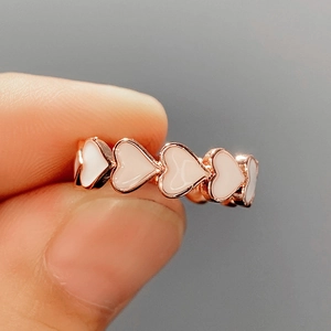 Détail d'une bague en or rose avec cœurs entrelacés et incrustation d'émail blanc