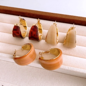 Vue détaillée de trois paires de boucles d'oreilles créoles en résine ambre et crème