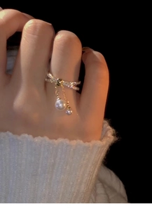 Close-up of gold-plated crossover bow ring with pavé stones and dangling pearls