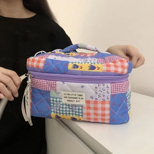 Detail of a quilted patchwork cosmetic bag featuring cherry patterns and a soft purple handle