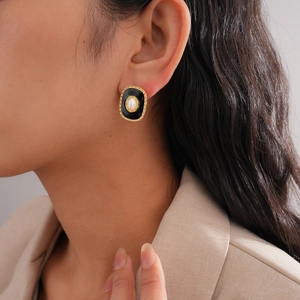 Close-up of vintage oval stud earring with pearl, black enamel and gold woven texture