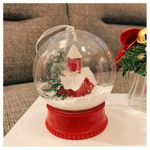 Close-up of a Christmas snow globe featuring a red house, green tree, and red base with light