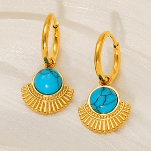 Detail of gold hoop earrings with turquoise stones on a soft beige textured fabric