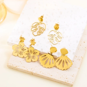 Detail view of gold stainless steel earrings featuring monstera leaf and shell designs