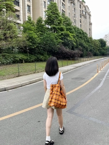 Outdoor lifestyle shot of a woman carrying a large orange plaid canvas tote bag