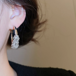 Close-up of sparkling silver hoop earrings with diamond inlay worn by a model