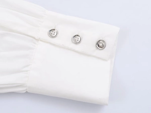 Detail of white poplin shirt cuff with three silver-grey buttons and fine fabric texture