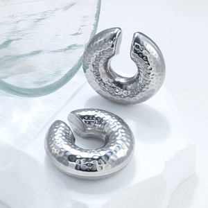 Macro detail of silver C-shape hammered earrings displayed on a white textured stone