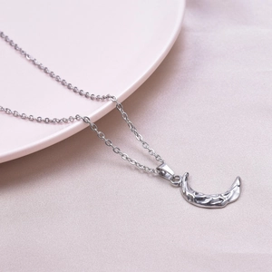 Macro view of silver crescent moon pendant with hammered texture on a dainty cable chain