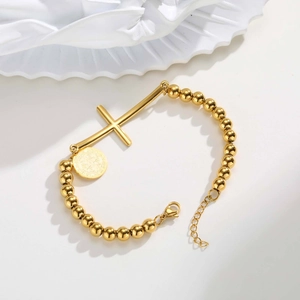 Detail of gold beaded bracelet featuring cross and medallion charms with lobster clasp