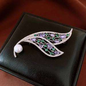 Macro shot of leaf brooch with white pearls and colorful zircon stones on satin