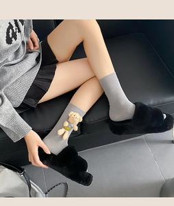 Detail of gray knit cotton socks with 3D plush bear and fuzzy black slippers on model