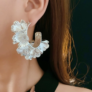 Macro shot of large silver floral C-shaped metal earrings worn by a female model
