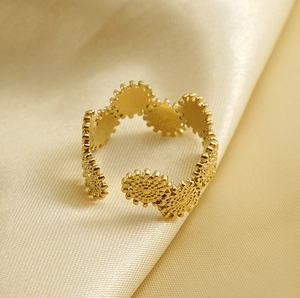 Detailed view of gold gear-shaped stainless steel open ring on soft satin fabric