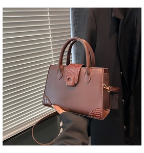 Detail of a dark brown square handbag with crocodile texture and arched handle in office setting
