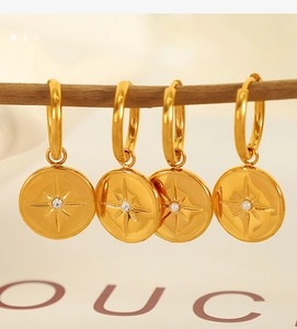 Macro detail of gold hoop earrings with starburst coin charms on a natural wood branch