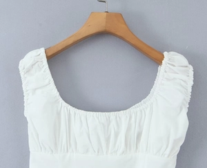 Detailed view of the square neckline with ruffled edges on a white cotton dress