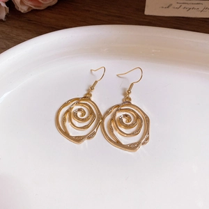 Gros plan de boucles d'oreilles roses dorées ajourées dans un plat en céramique blanc