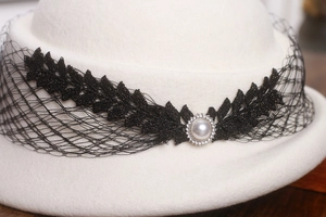 Détail d'un béret en laine blanche avec dentelle noire, perle et cristaux brillants