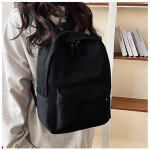 Side view of a minimalist black nylon backpack worn by a model in a lifestyle setting