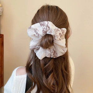 Close-up of a large cream fabric hair scrunchie with brown floral print on a high ponytail