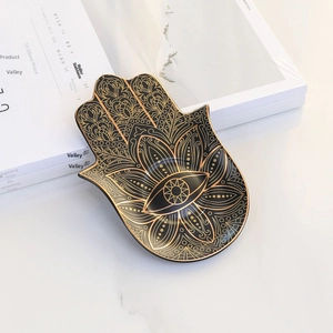 Macro shot of black ceramic Hamsa Hand jewelry tray with gold Evil Eye detail and glossy finish