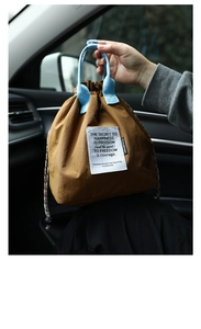 Detailed close-up of brown nylon drawstring lunch bag with light blue fabric handles