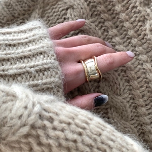 Close-up of a wide wavy gold ring worn with a beige chunky knit sweater for autumn