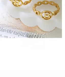 Close-up of golden letter B hollow ring with chain-link band on decorative tray