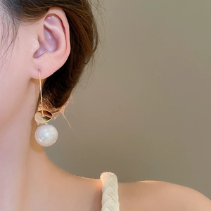Close-up of elegant gold hook earring featuring a round sequin and lustrous white pearl