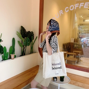 Detail of beige canvas tote bag with beloved embroidery in a lifestyle cafe setting