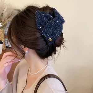 Detail view of navy blue tweed bow hair claw with gold button on an elegant hairstyle